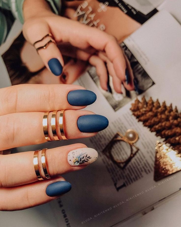 Chic Matte Navy Nail Design with Floral Accent and Elegant Gold Rings.