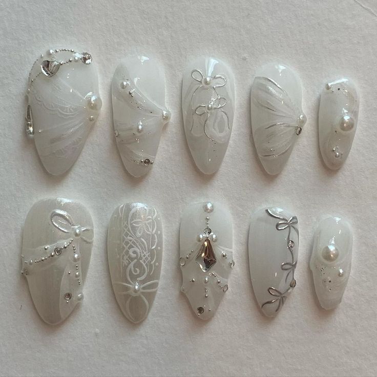 Sophisticated White Nail Design with Delicate Embellishments and Intricate Silver Patterns.