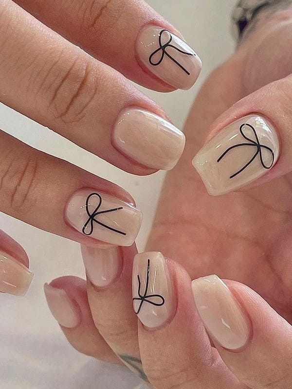 Chic Elegant Nude Nails Adorned with Playful Black Bow Designs.