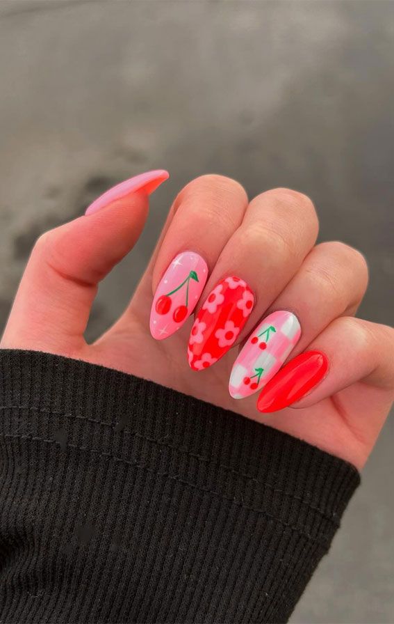 Vibrant Floral Nail Design: A Playful Mix of Cherry Motifs and Bright Reds on Soft Pink Backgrounds.