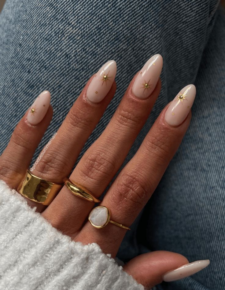 Chic Almond-Shaped Nails with Gold Star Accents and Nude Polish for Effortless Elegance.