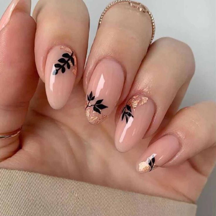 Sophisticated Nude Nail Design with Black Leaf Patterns and Glamorous Gold Flakes.