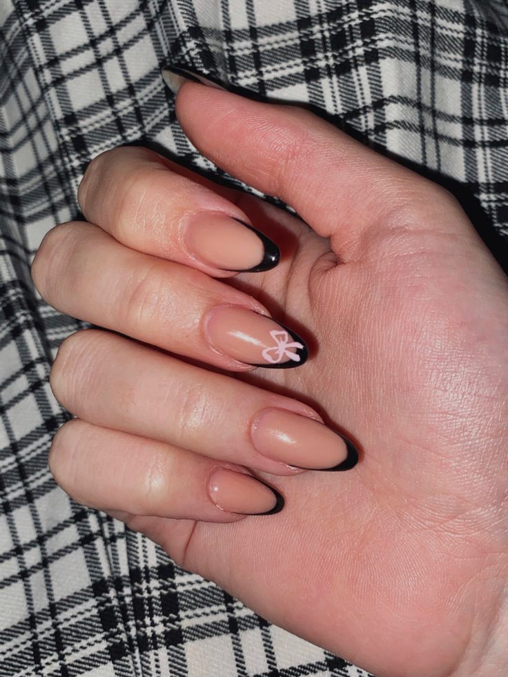 Chic Nail Design: Natural Nude Base with Black Tips and Playful White Bow Accent.