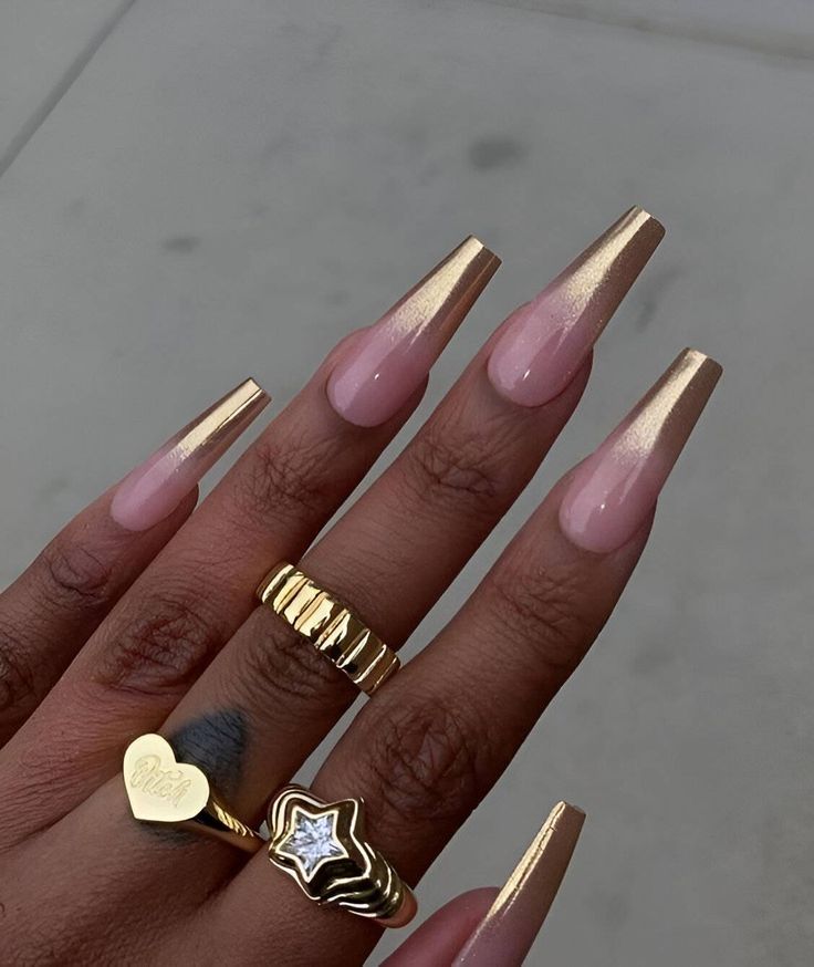 Sophisticated Soft Pink Stiletto Nails with Shimmering Gold Accents and Stylish Gold Rings.