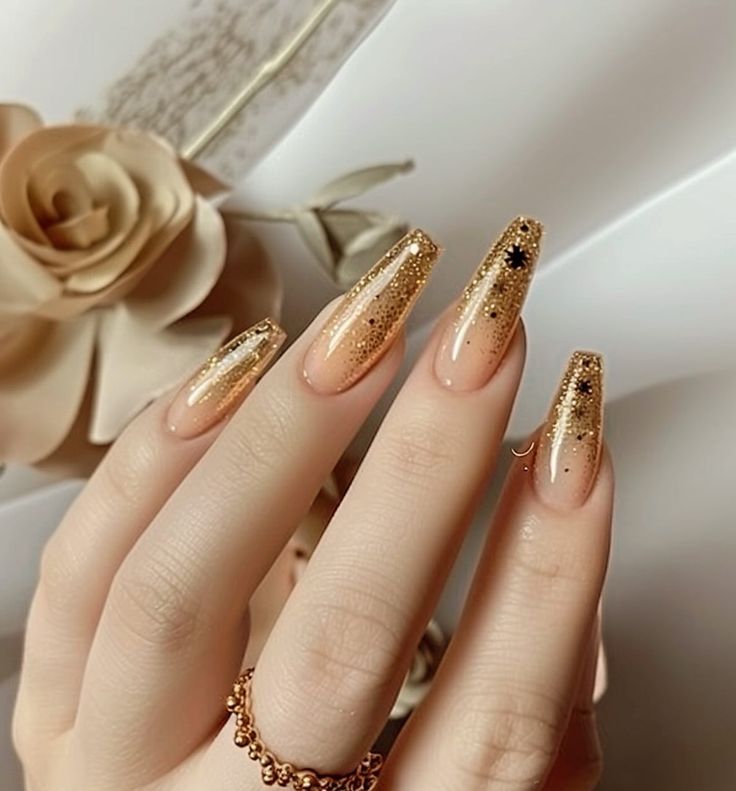 Elegant Nude and Gold Glitter Nail Design with Black Star Accents.