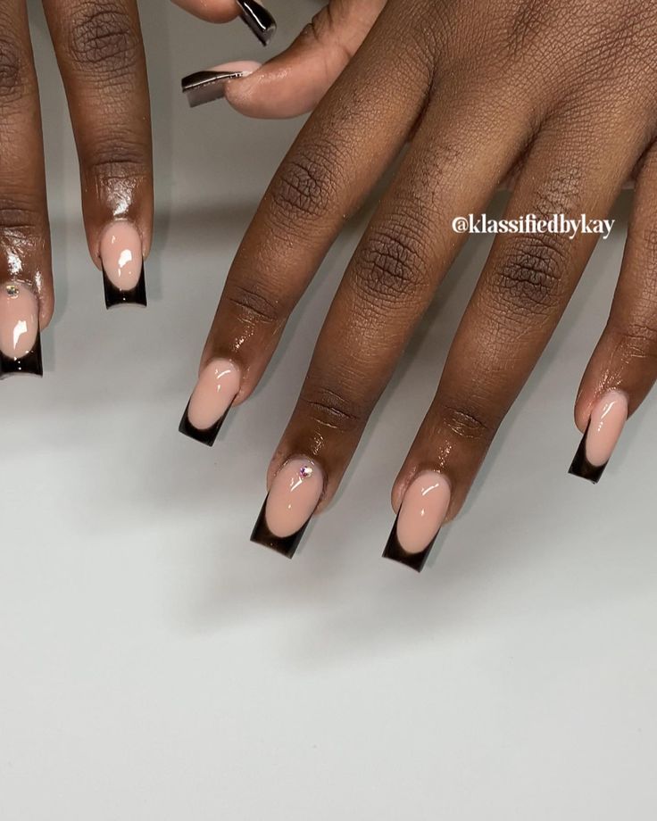 Sophisticated Nude and Black Square Nail Design with Glossy Finish and Elegant Embellishments.