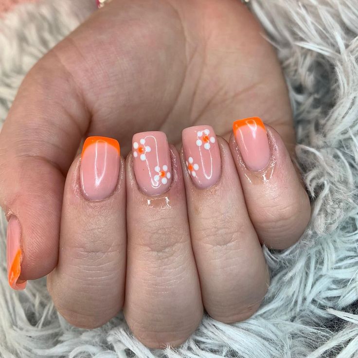 Chic Summer Nail Design: Soft Pink Base with Vibrant Orange Tips and Delicate White Floral Accents.