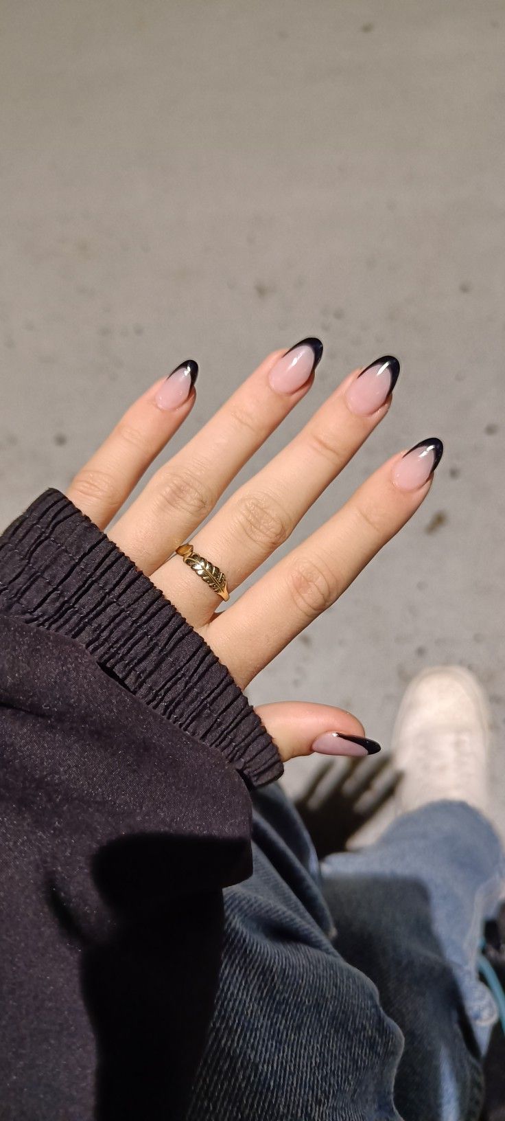 Sophisticated Almond-Shaped Nail Design: Nude Base with Striking Black Tips and Chic Gold Ring Accent.