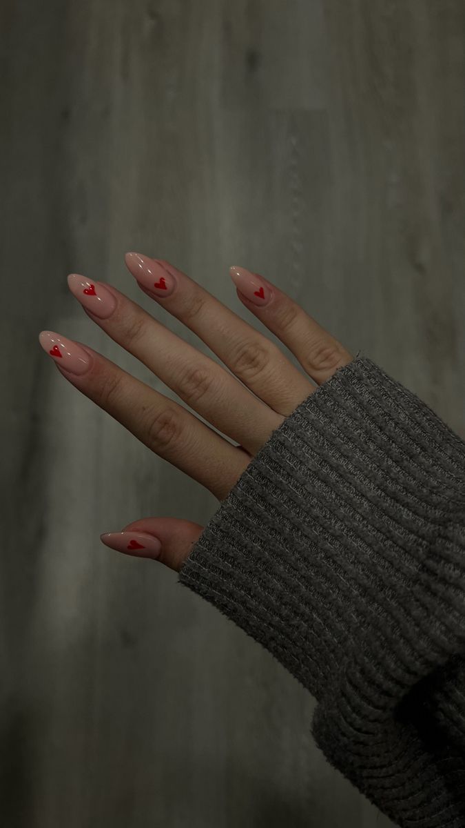 Chic Nude Nail Design with Playful Red Heart Accents Paired with a Cozy Gray Sweater.