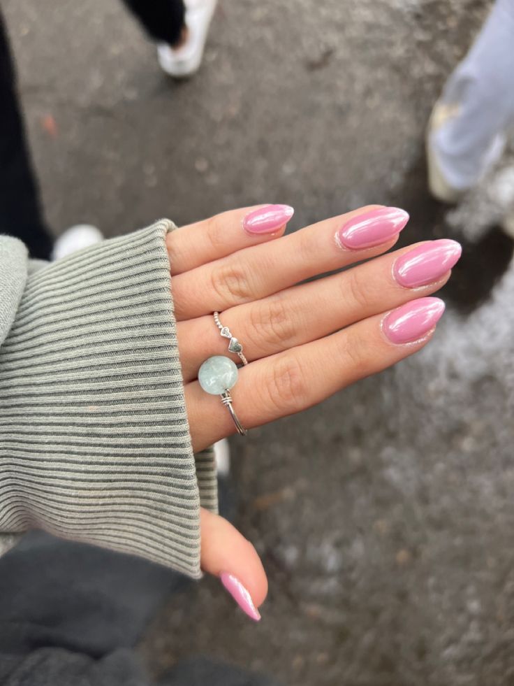 Chic Almond Pink Nails with Glossy Finish and Delicate Rings for a Cozy Yet Elegant Look.