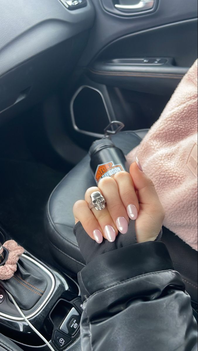 Sophisticated Nude Nails with Glossy Finish and Bold Skull Ring in Cozy Car Interior.