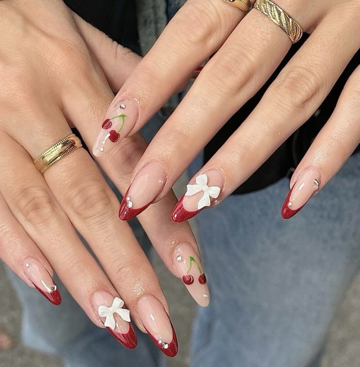 Chic Nail Design: Bold Red Tips, Delicate Nude Accents, Cherry Motifs, Floral Details, and Rhinestone Enhancements.