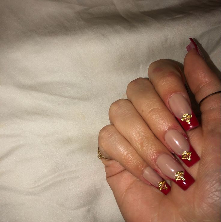 Sophisticated Nude and Deep Red Nail Design with Glamorous Gold Embellishments.