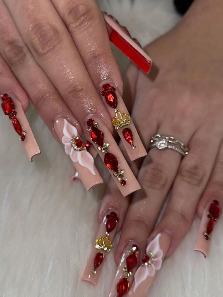 Elegant Long Tip Nail Design with Red Gemstones, Floral Details, and Gold Accents for Glamorous Occasions.