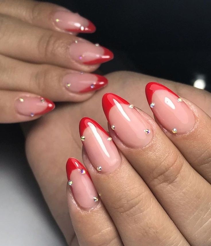 Chic French Tip Nail Design: Bold Red Tips and Elegant Nude Base with Rhinestone Accents.