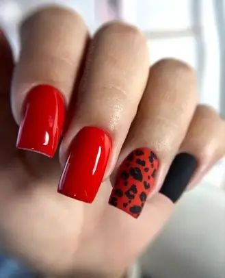 Striking Manicure: Vibrant Red and Black Nails with Playful Leopard Print Accent.