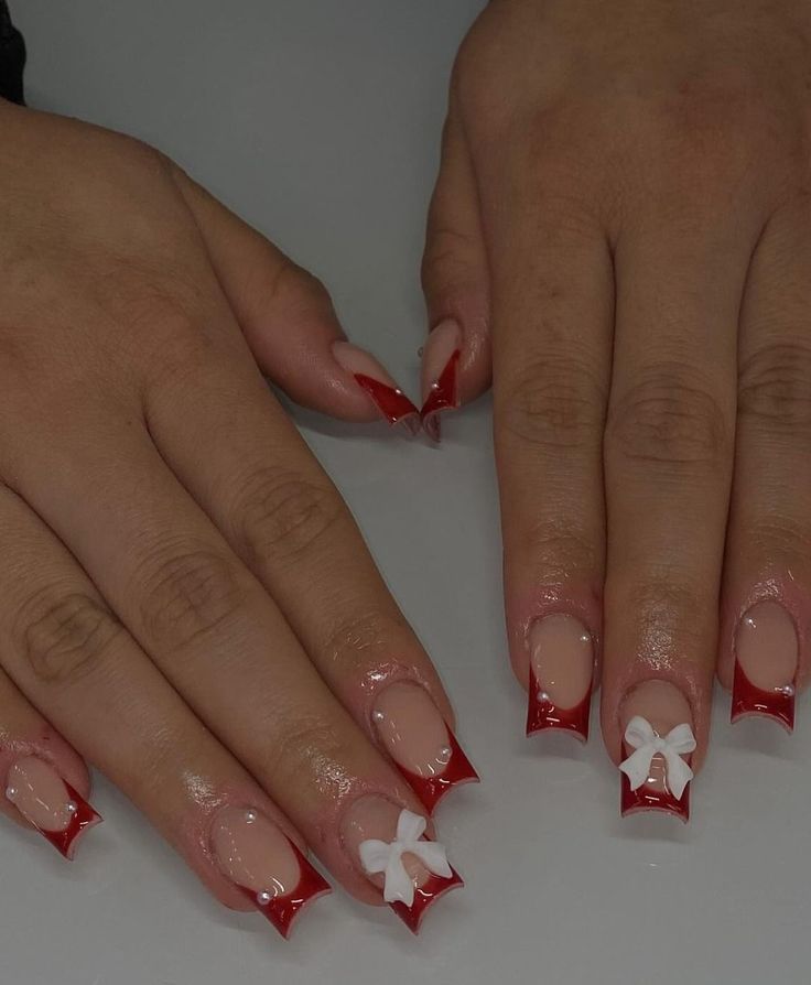 Chic Nude and Bold Red Nail Design with Playful White Bow Accents.