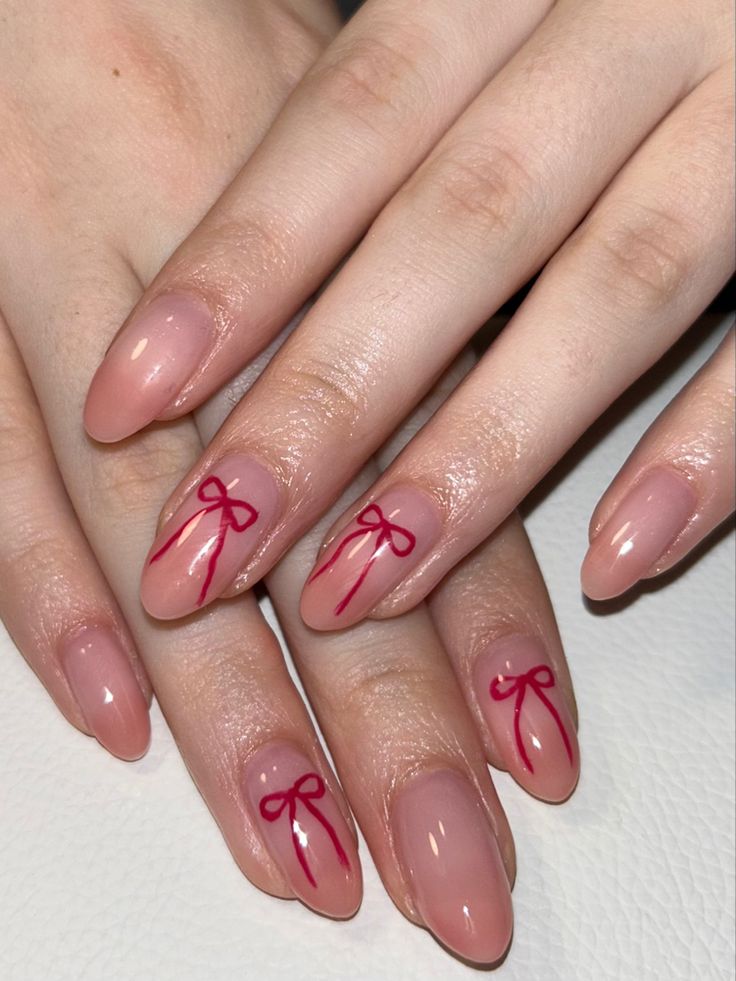 Whimsical Nail Art: Soft Nude Base with Delicate Red Ribbon Bows for Charming Elegance.