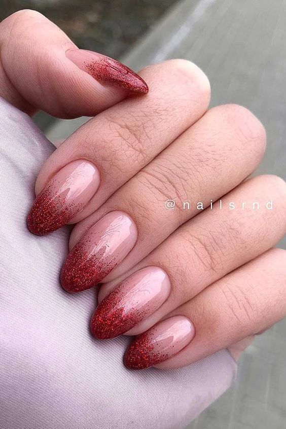 Sophisticated Almond-Shaped Ombre Nail Design: Soft Nude Base to Glittery Red Tips.