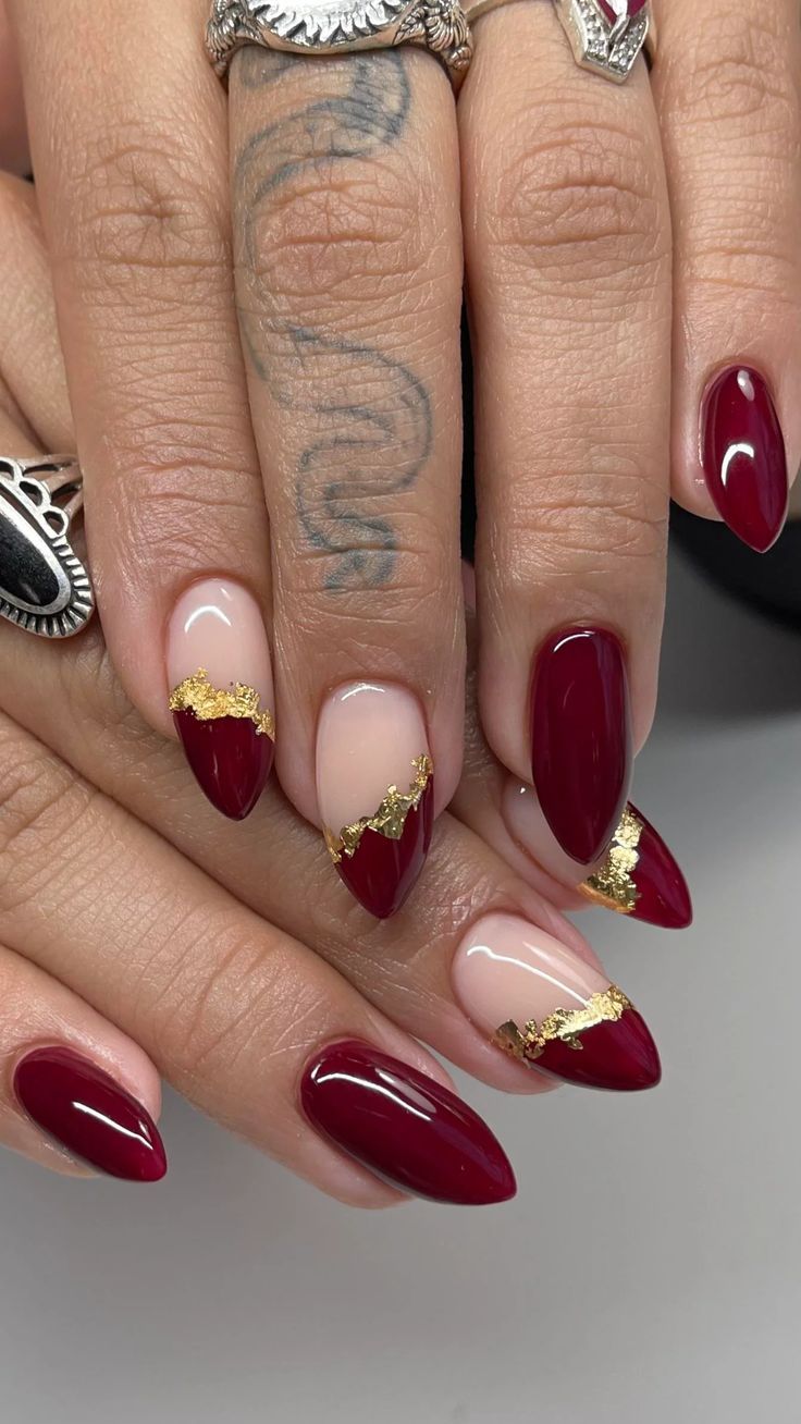 Striking Burgundy and Nude Nail Design with Gold Leaf Accents for a Glamorous Statement.