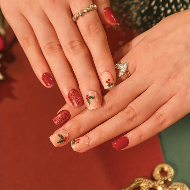 Elegant Festive Nail Design: Glossy Red, Shimmering Glitter, and Holly Motifs Enhanced by Metallic Jewelry.