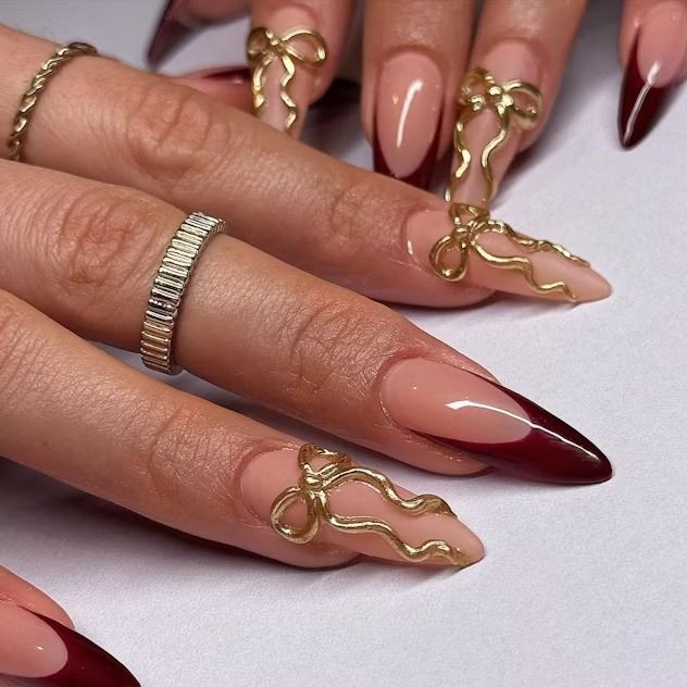 Elegant Almond-Shaped Nail Design: Striking Nude and Deep Red with Gold Ribbon Accents.