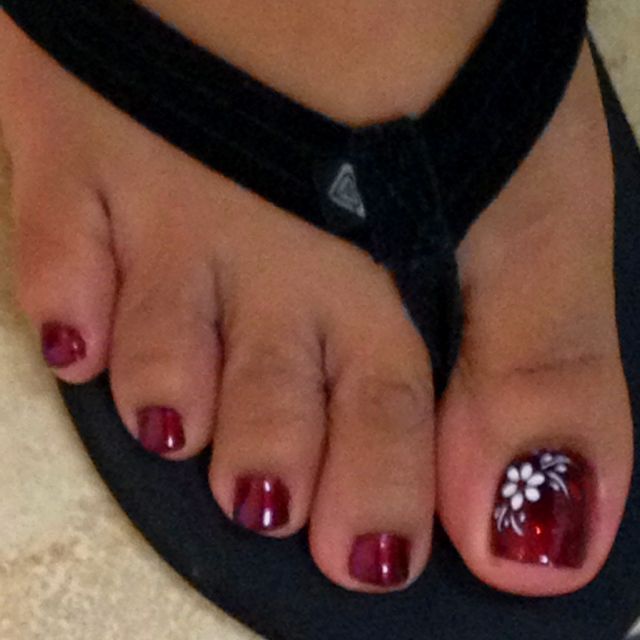 Sophisticated Red Toenail Design with Glossy Finish and Floral Accent.