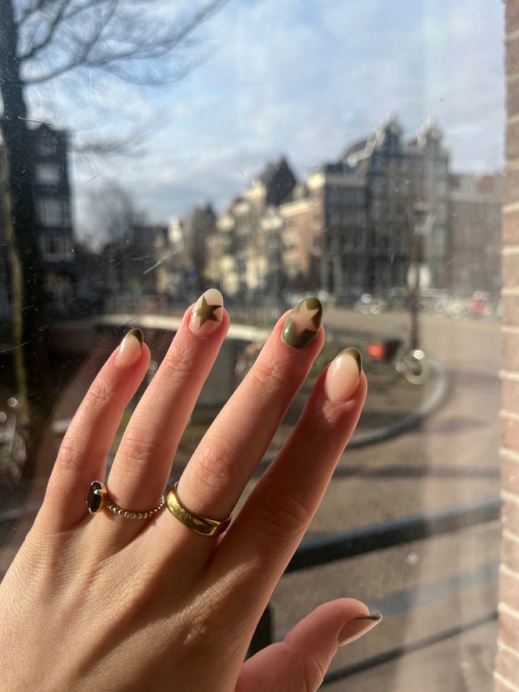 Stylish Nail Design: Elegant Nude and Olive Green Shades with Star Motifs Against an Urban Backdrop.