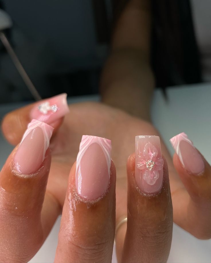 Elegant Soft Pink Nail Design with Intricate White Swirls and Glam Floral Accents.