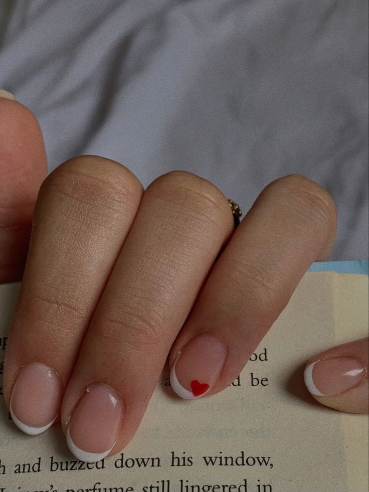 Charming French Manicure with Subtle Nude Base, Delicate White Tips, and Playful Red Heart Accent.