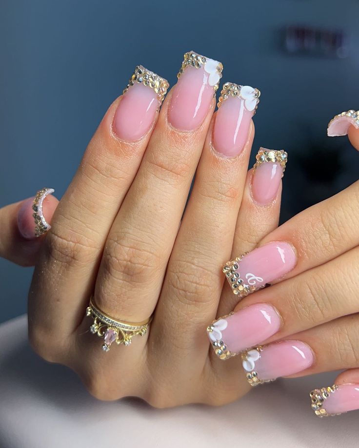 Sophisticated Light Pink and Gold-Tipped Nail Design with Floral Accents and Rhinestones.