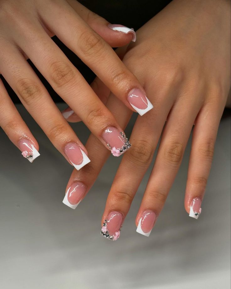 Sophisticated Nail Design: Soft Pink French Tips with Floral Accents and Sparkling Embellishments.