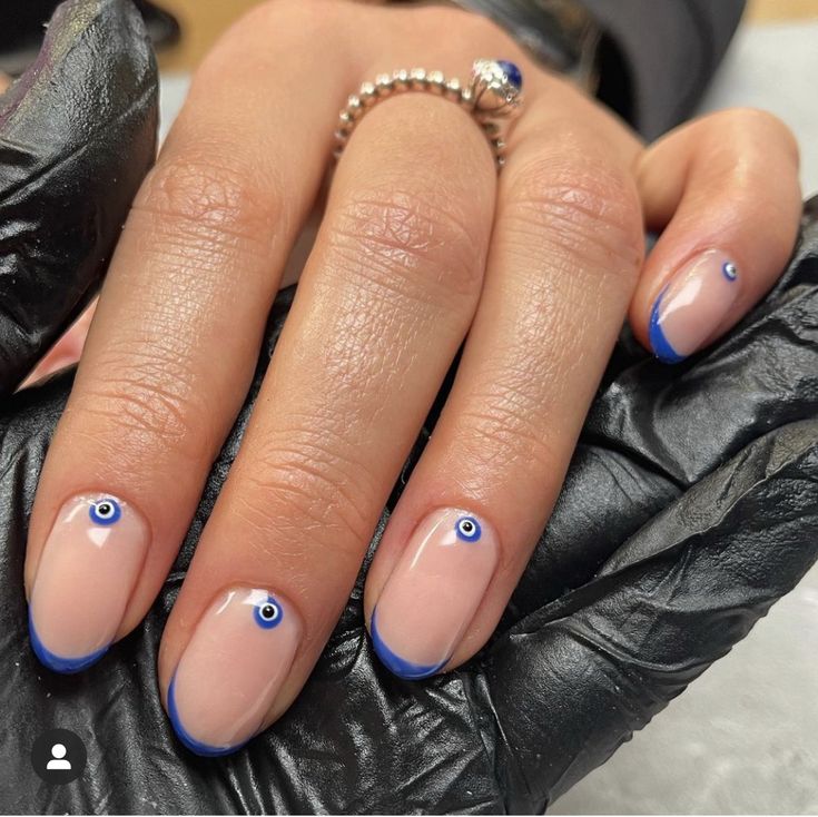 Chic Nude Nail Design with Bold Blue Tips and Unique Eye Motifs.