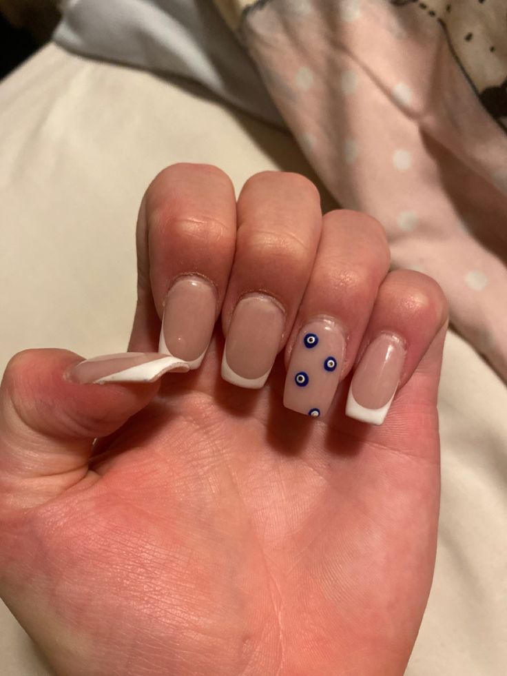 Stylish Nude and White Nail Design with Playful Blue Eye Accent.