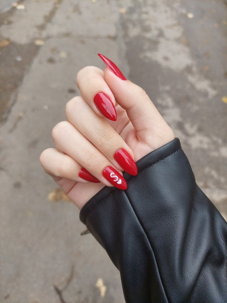 Elegant Glossy Red Almond Nail Design with Whimsical Accent, Perfectly Paired with a Sleek Black Leather Jacket.