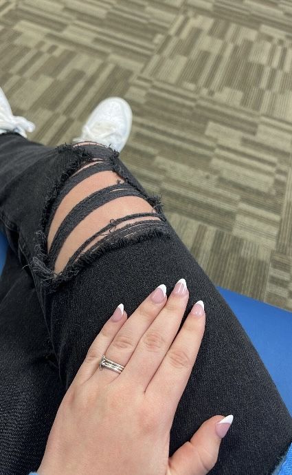 Sophisticated French Tip Nail Design Complements Distressed Black Denim for a Chic Look.