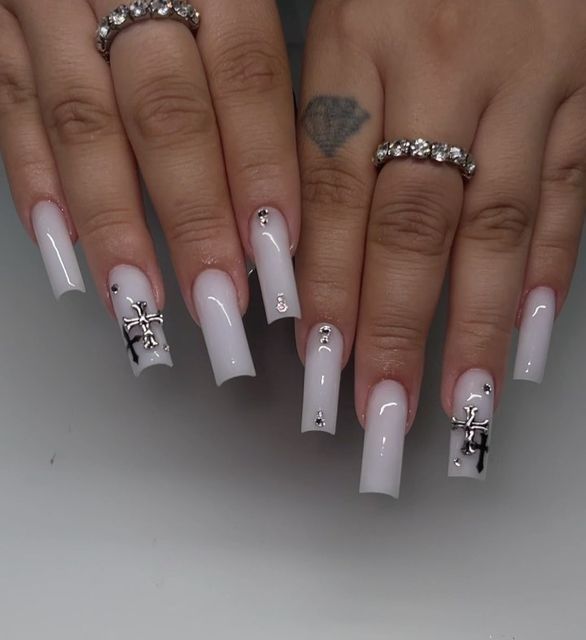 Chic Long Nude Nail Design with Silver Cross Accents and Rhinestones for a Glamorous Statement.