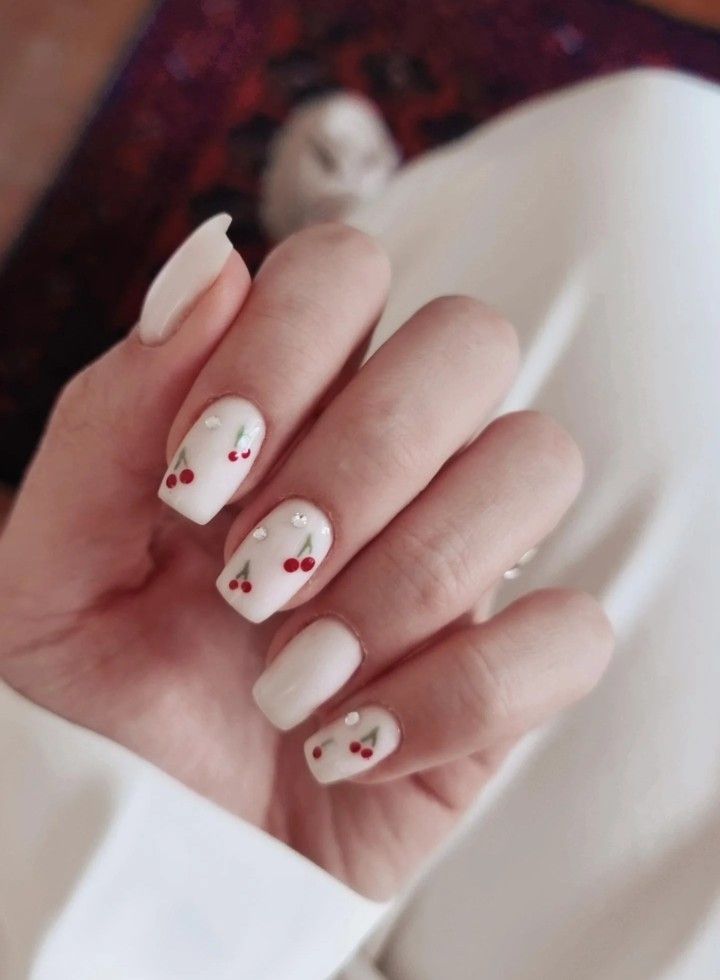 Charming Cherry Nail Design: Soft White Base with Delicate Rhinestone Accents.