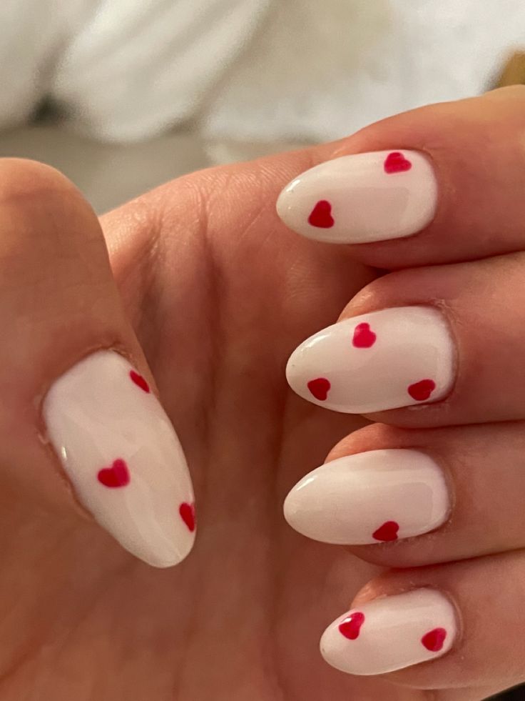 Charming Milky White Nail Design with Tiny Red Heart Accents for Romantic Occasions.