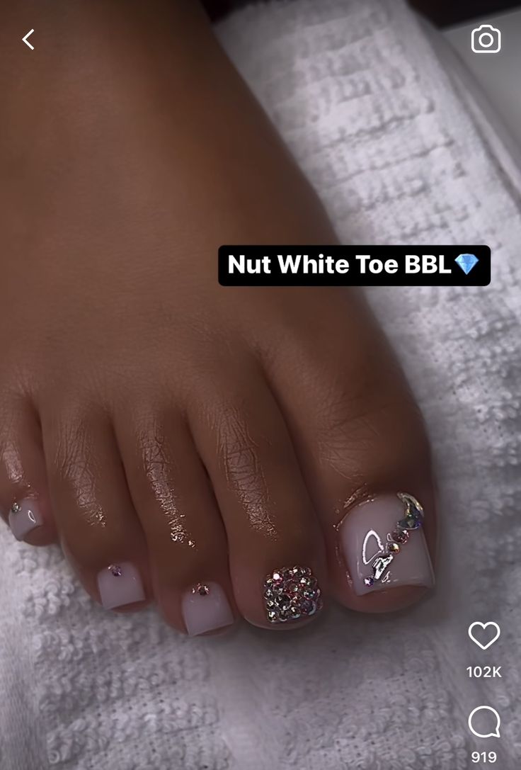 Elegant Soft Nut White Toe Nail Design with Glitter Accent and Gemstone Pattern.