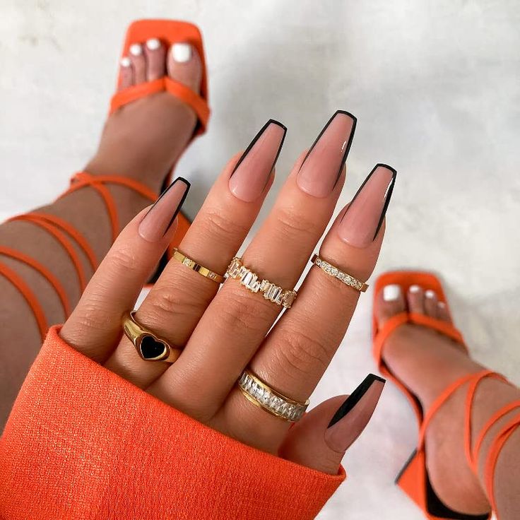 Chic Nail Art with Nude Base and Black Tips, Paired with Gold and Silver Rings and Vibrant Orange Footwear.