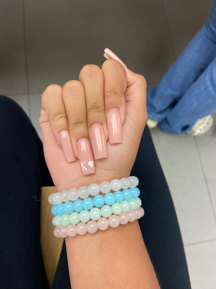 Chic Soft Pink Nail Design with Heart Accent and Colorful Bracelet Pairing.