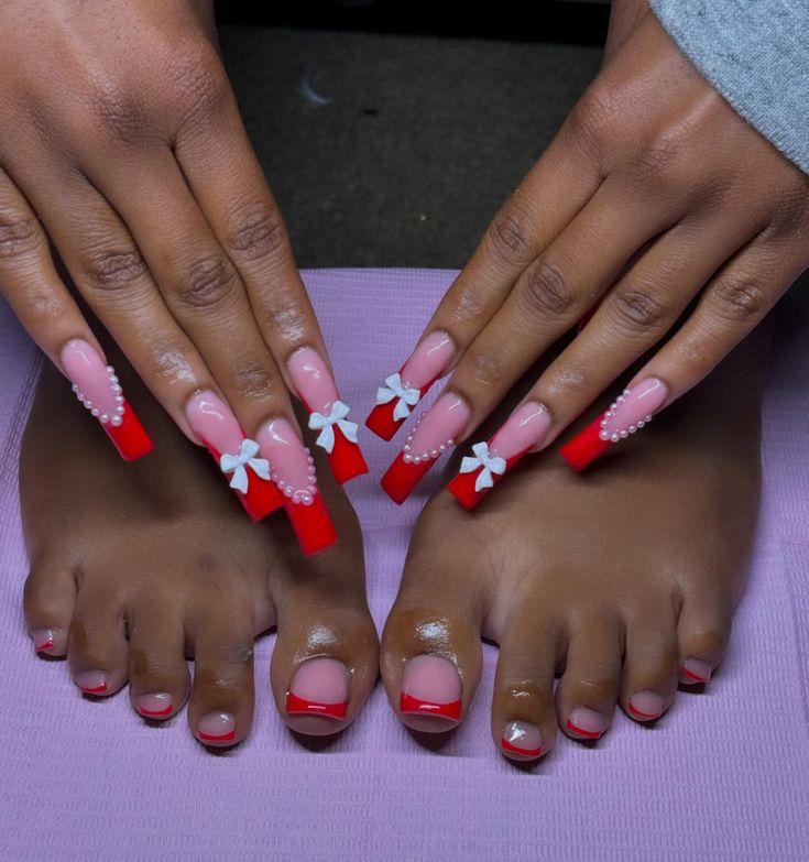 Glamorous Red-Tipped Nail Design with Soft Pink Base and Pearl-Embellished Bows.