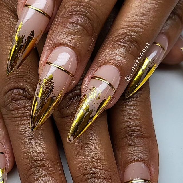 Elegant Nude and Gold Stiletto Nails with Intricate Artistic Accents and Polished Stripes.