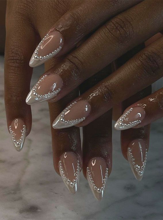 Sophisticated Stiletto Nails with Soft Nude and Shiny White Hues Adorned with Delicate Pearl Embellishments.