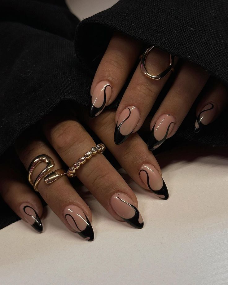 Chic Nail Design: Nude Base with Sleek Black Tips and Artistic Swirls Accentuated by Gold Rings.