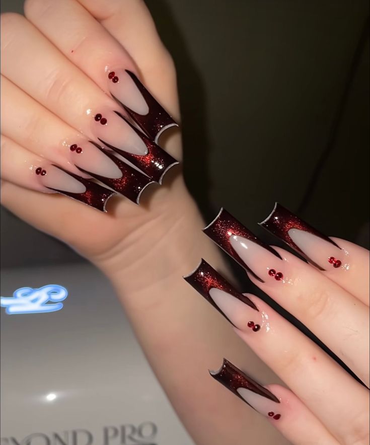 Dramatic Burgundy and Nude Nail Design with Intricate Shapes and Elegant Red Gems.