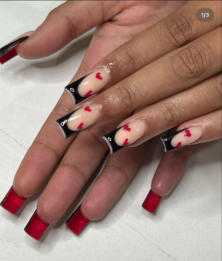 Playful Nail Design: Nude and Red Shades with Heart Motifs and Black Tips.