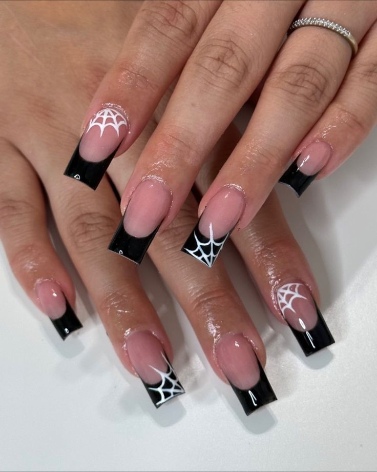 Edgy Halloween Nail Design: Glossy Black Tips with Intricate White Spiderweb Patterns on a Nude Base.