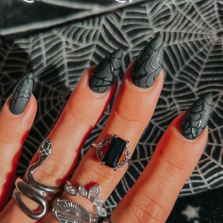 Dramatic Gothic Nail Art: Black Stiletto Design with Spider Web Patterns and Silver Ring Accents for a Mystical Fall Aesthetic.